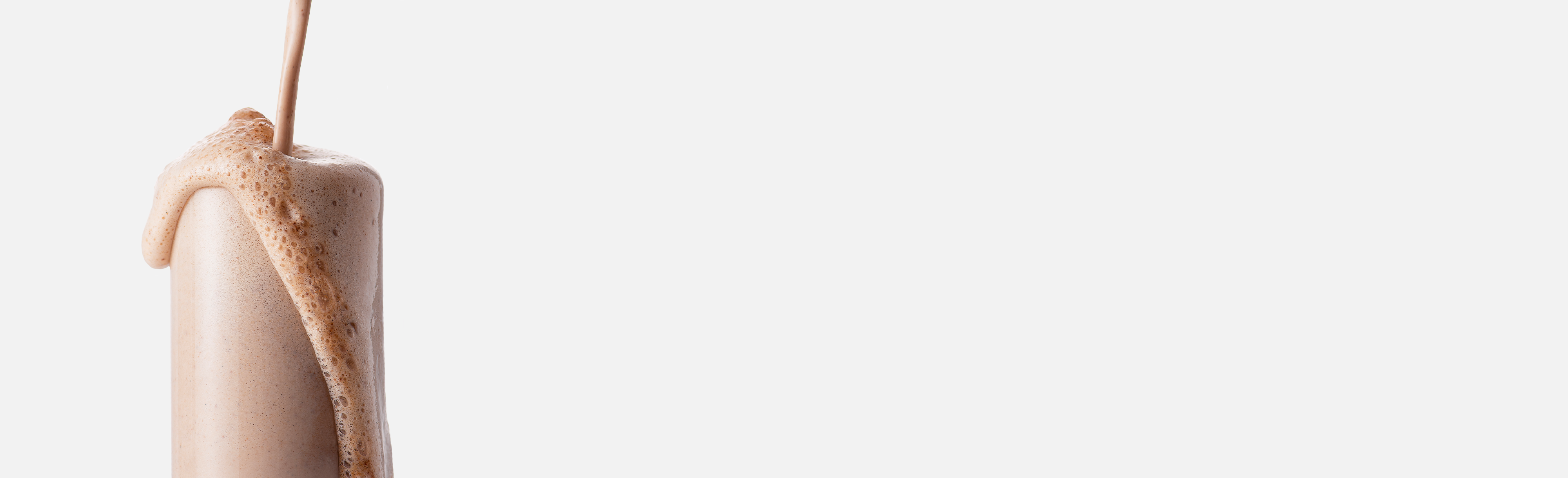 White background with a clear glass and ARMRA performance revival chocolate product being poured in